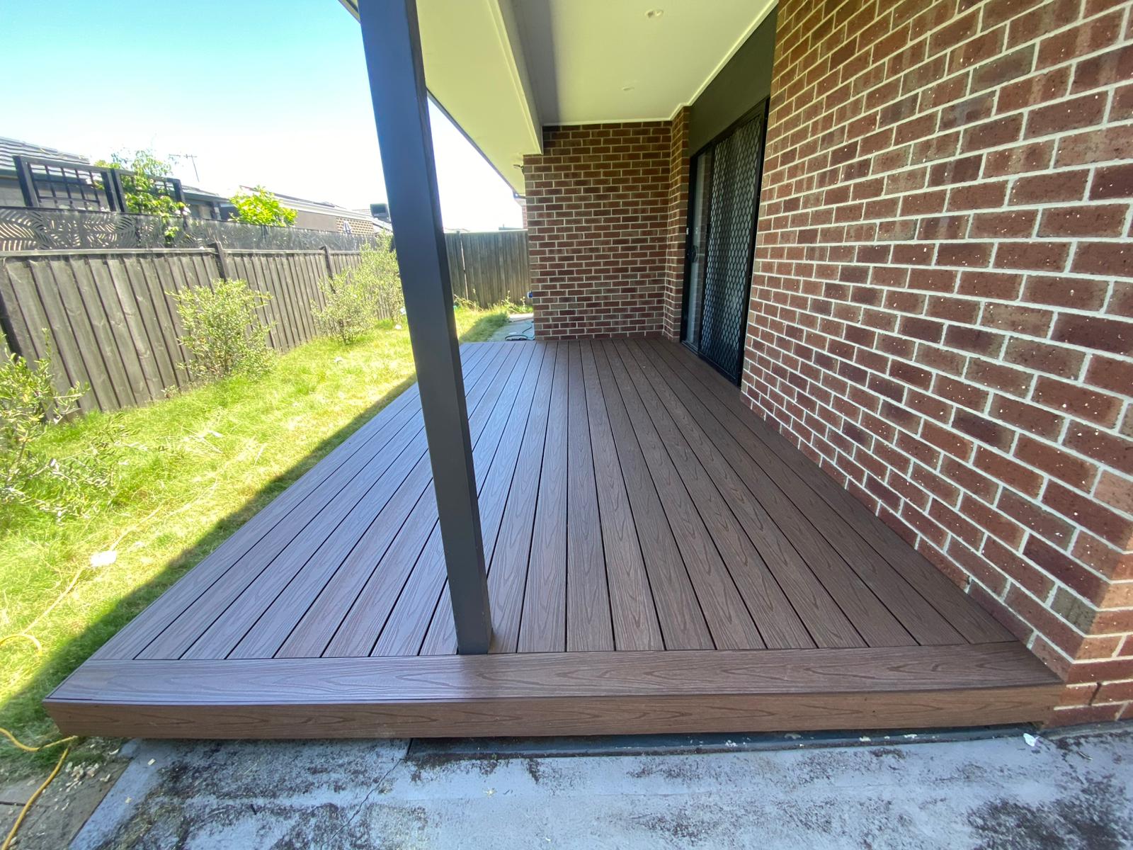 Chocolate composite deck under a verandah beside a brick home